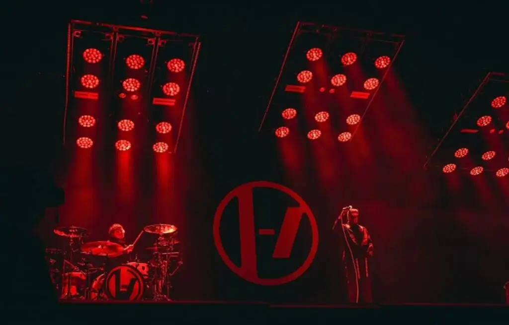 Josh e Tyler performando lado com o símbolo da banda entre eles e holofotes vermelhos os iluminando. Foto com ângulo próximo ao palco com ângulo direcionado para cima